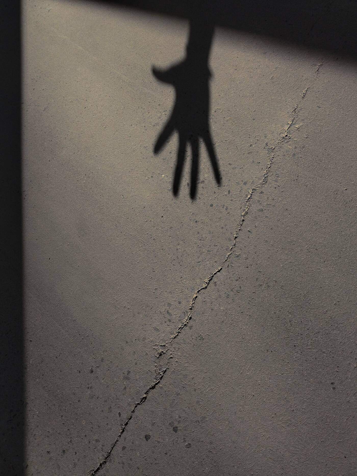 A shadow of a hand reaching down a cracked wall